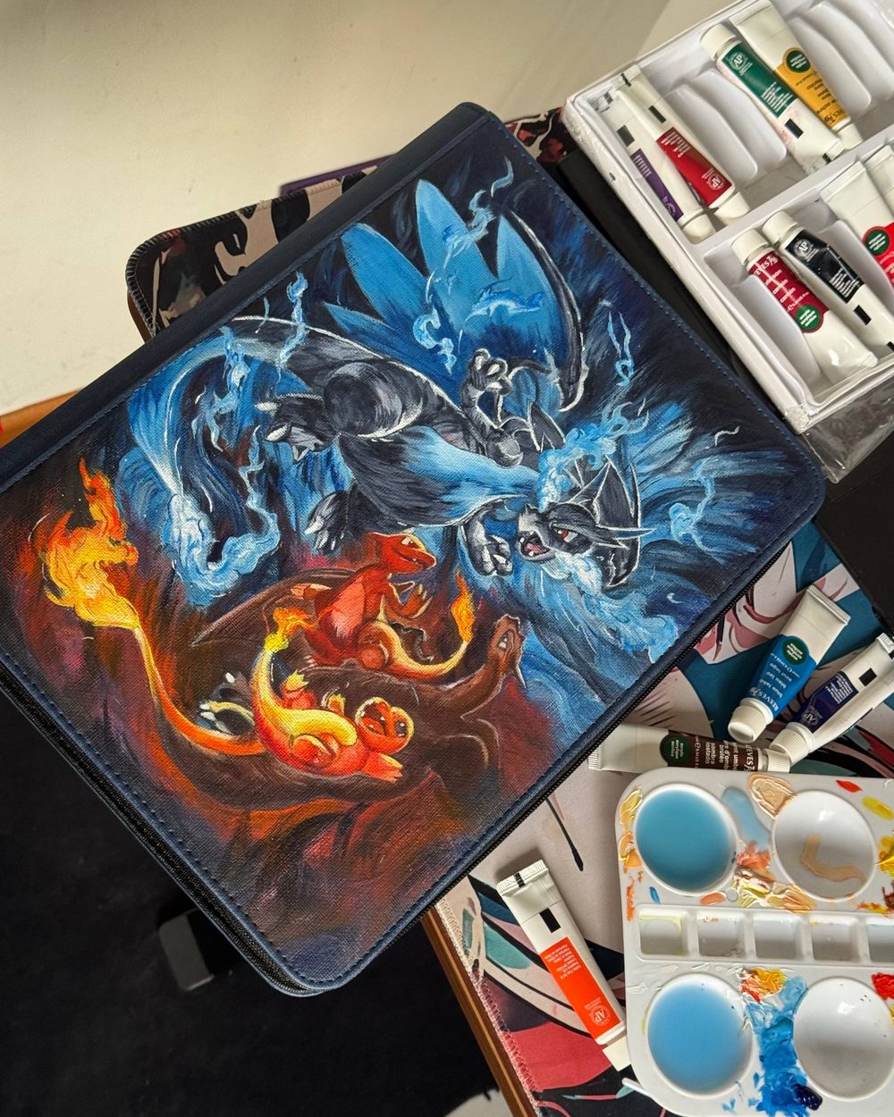 Hand-painted Mega Charizard binder beside the paints it was made with